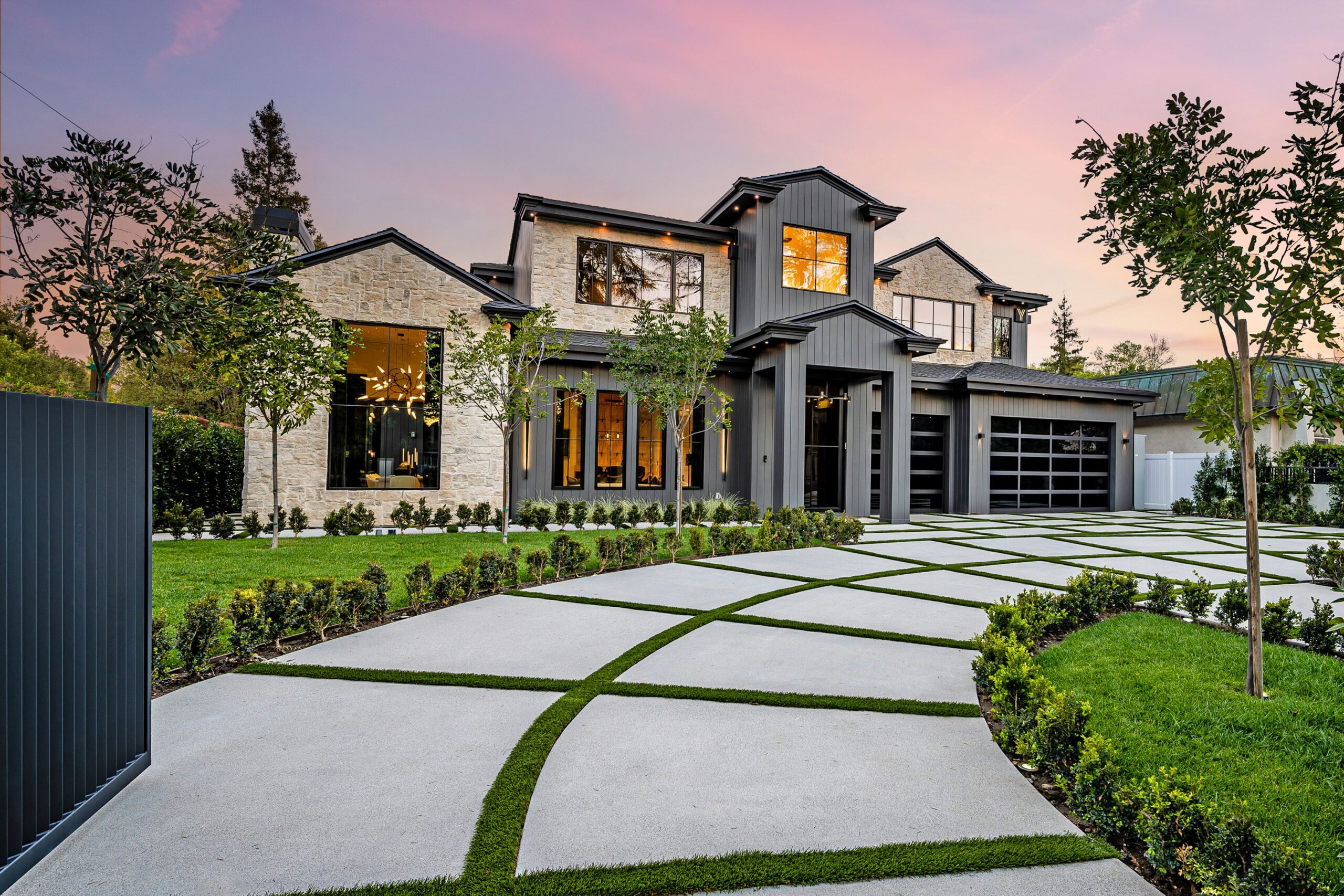 Modern luxury home with geometric driveway and sunset sky.